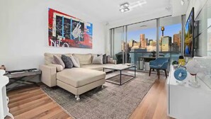Ein modernes Wohnzimmer mit einer Couch, einem Couchtisch und Blick auf die Stadt durch große Fenster.