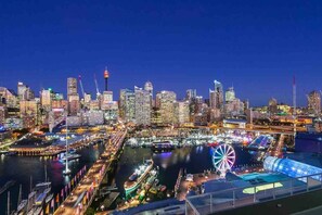 A nighttime cityscape with illuminated buildings, a Ferris wheel, and a harbor with boats.