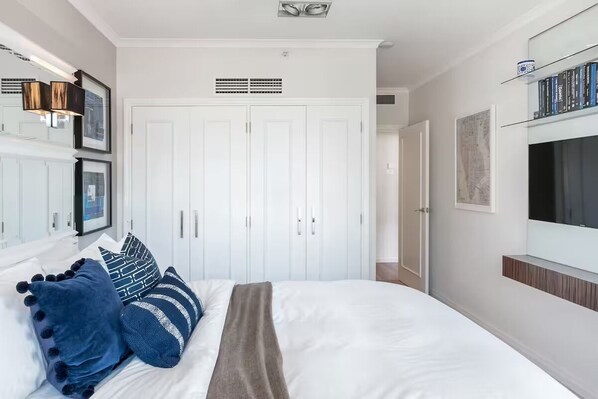 A bedroom with a large bed, white wardrobe, and a TV on the wall.