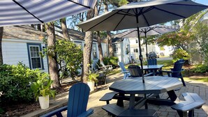 Un patio con tavoli e sedie da picnic, circondato da alberi e da una casa.