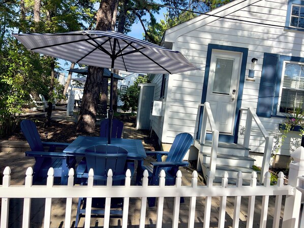 A white house with blue shutters, a covered patio with a table and chairs, and a white picket fence.