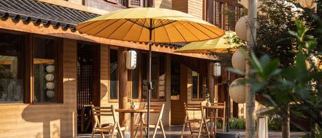 A traditional wooden building with a tiled roof, outdoor seating area with tables and chairs, and a wooden fence.