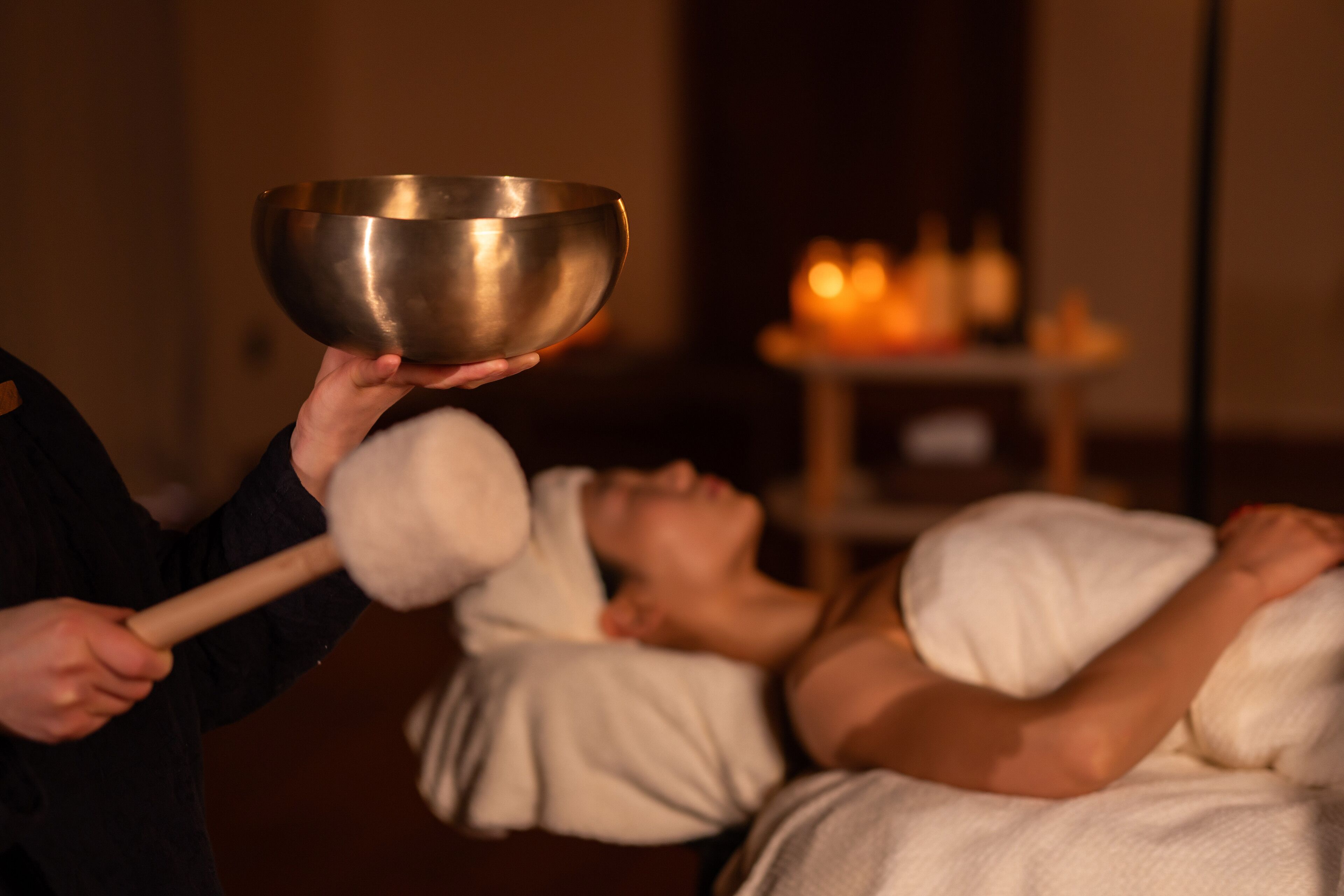 A person holding a metallic bowl over another person's head, with candles in the background.