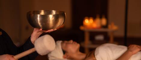A person holding a metallic bowl over another person's head, with candles in the background.