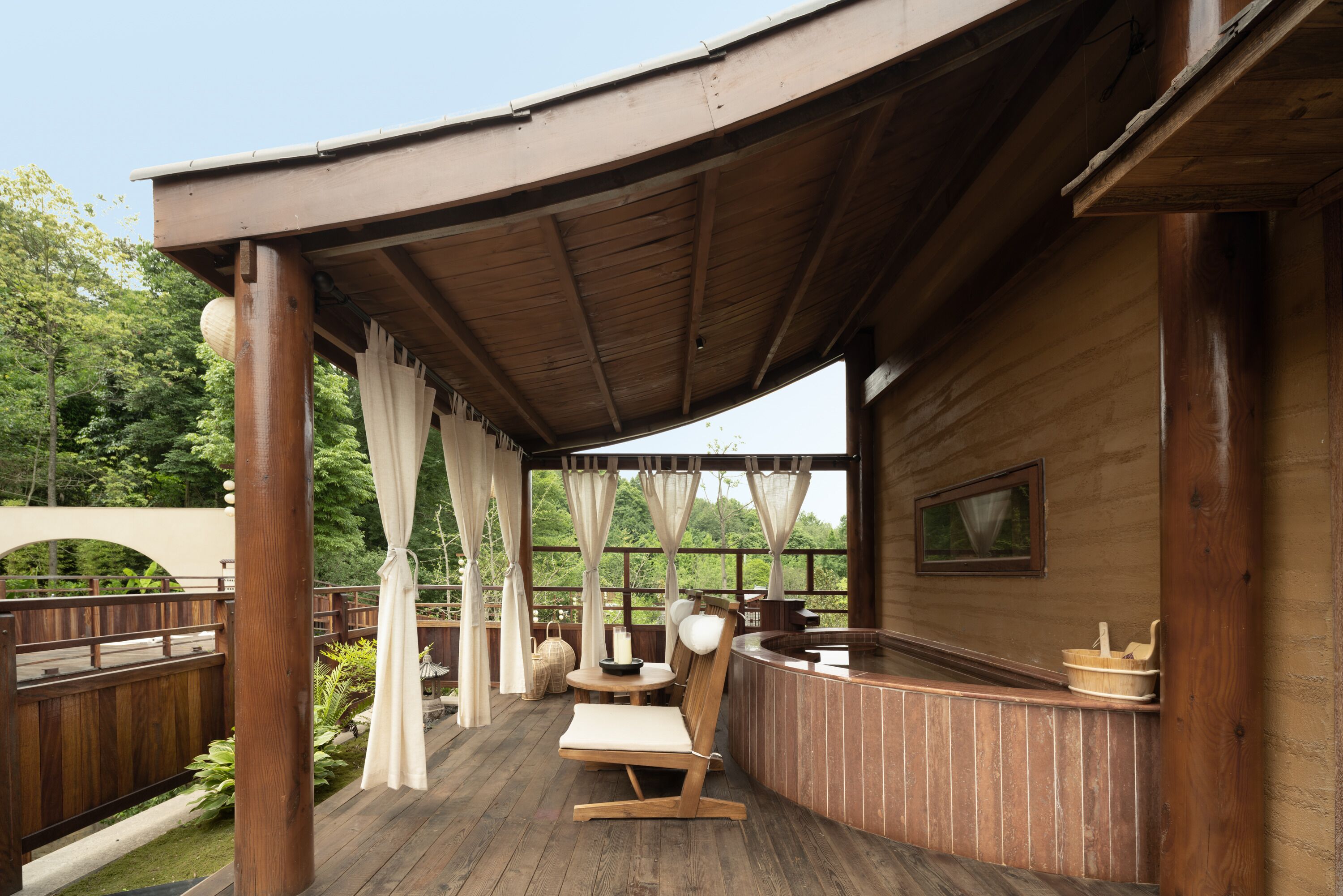 Una terraza de madera con techo curvo, un jacuzzi y una zona de estar con cojines.