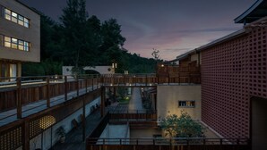 A multi-level wooden bridge connecting buildings in a courtyard with a view of trees and a sunset. - Hegu Mountain Retreat (Chengdu)
