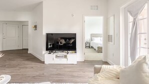 Un salon moderne doté d’un téléviseur à écran plat, d’un plancher en bois et d’un canapé blanc.