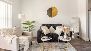 Un salon moderne avec un canapé gris, un fauteuil blanc, une œuvre d’art murale ronde encadrée d’or, une lampe sur pied et un miroir.