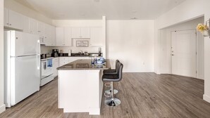 Une cuisine moderne avec des meubles blancs, un îlot central doté de tabourets de bar et un plancher en bois.