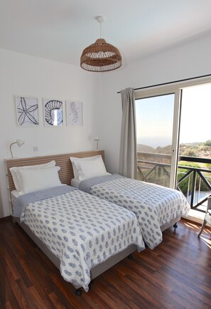 A bedroom with two beds, a large window with a view, and a hanging light fixture. - STAY Pantheon Villa (Pissouri)