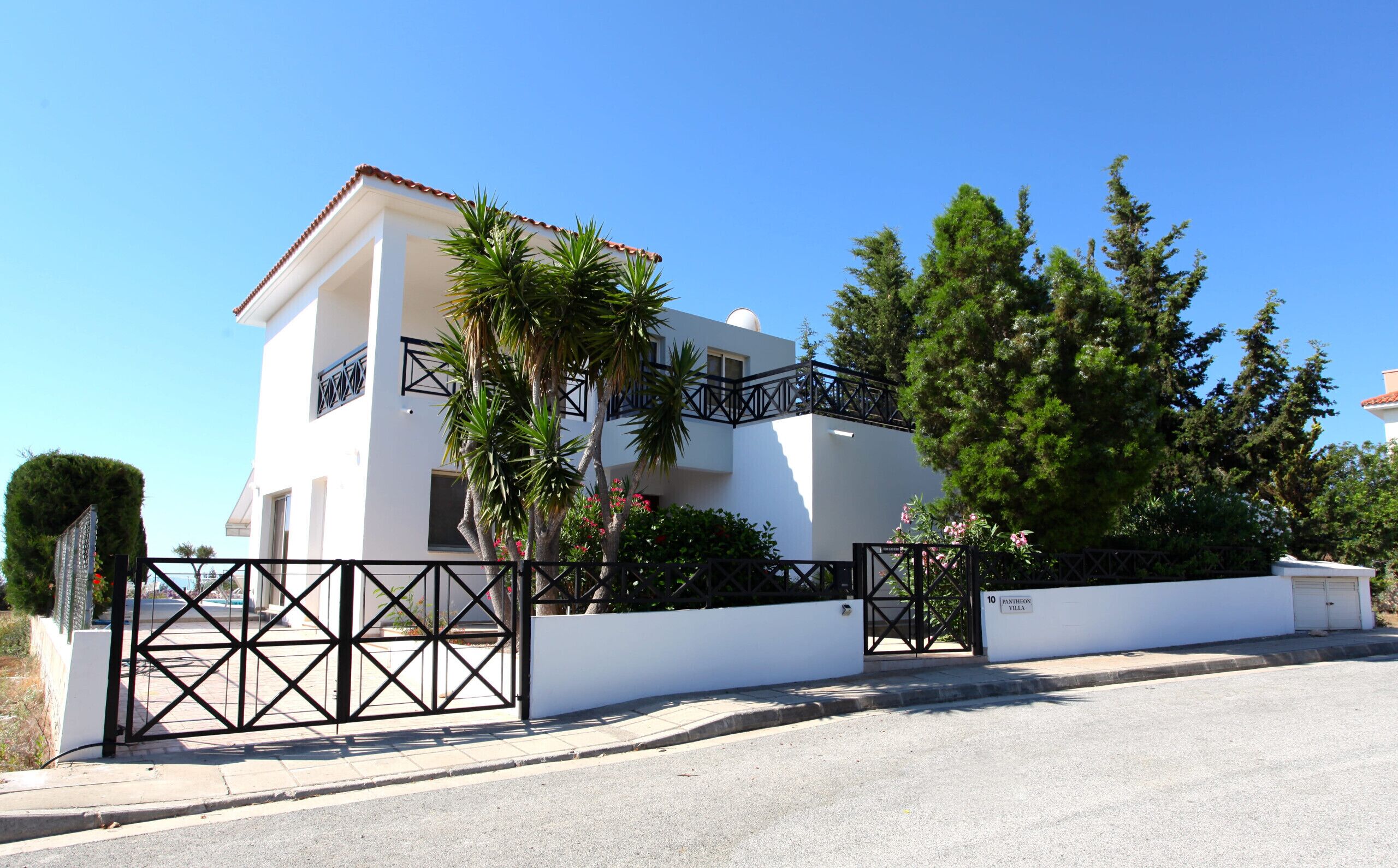 Uma vila de dois andares com fachada branca, uma varanda com guarda-corpo preto e um portão com design geométrico.