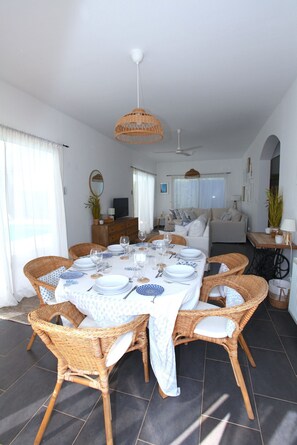 A dining area with a round table set for four, surrounded by wicker chairs. - STAY Pantheon Villa (Pissouri)