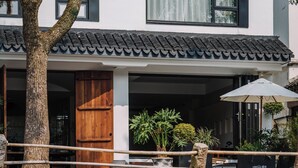 A traditional building with a tiled roof, a wooden door, and a stone railing overlooking a calm water body. - Shine on (Suzhou)