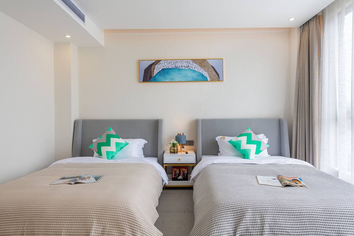 Una habitación de hotel con dos camas, una mesita de noche con lámpara y un cuadro en la pared.