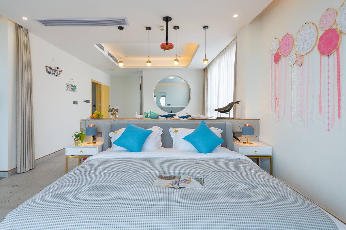 Una habitación de hotel moderna con una cama grande, mesitas de noche, un espejo y una pared decorada con arte.