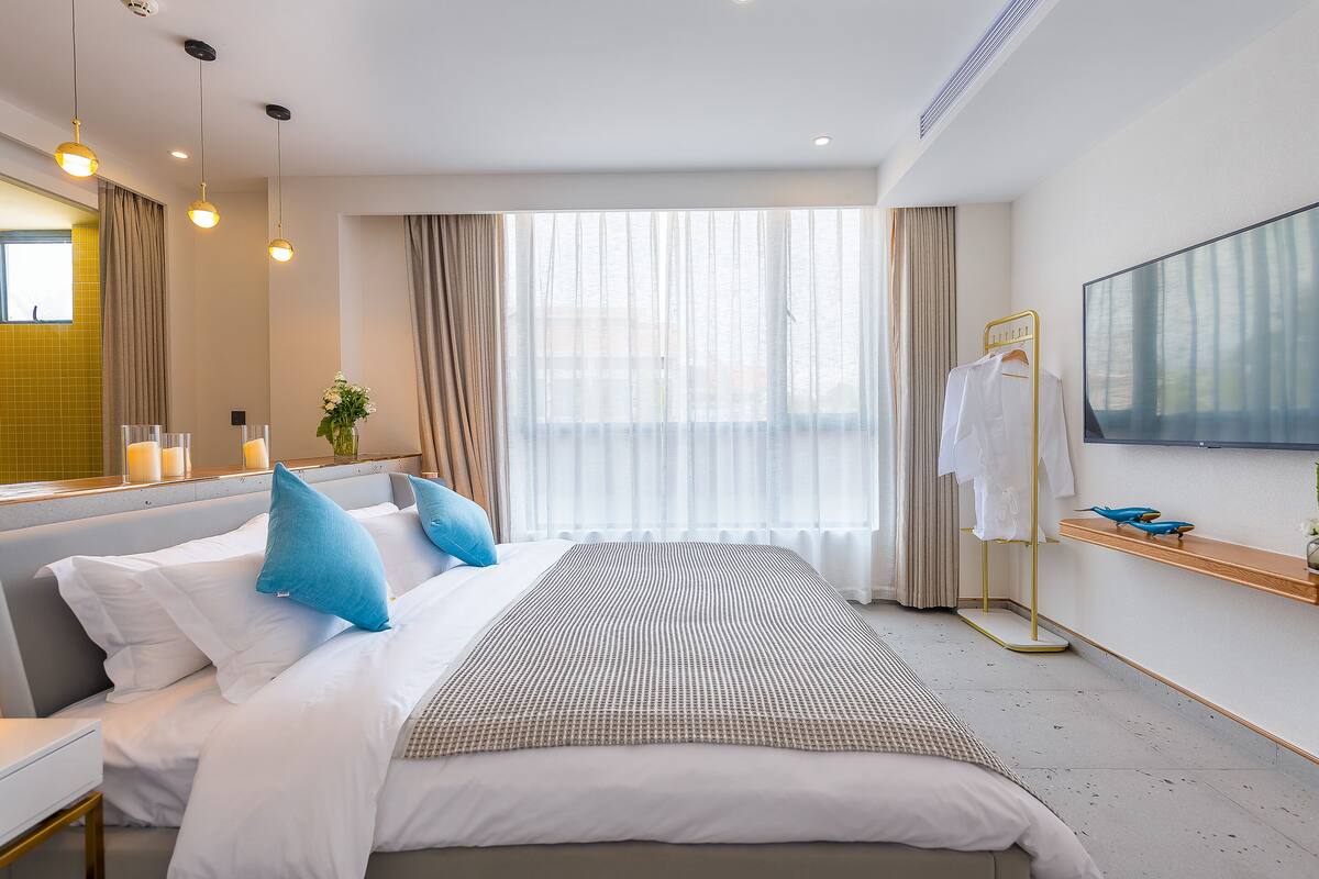 Una habitación de hotel con cama, mesita de noche y un amplio ventanal con cortinas.
