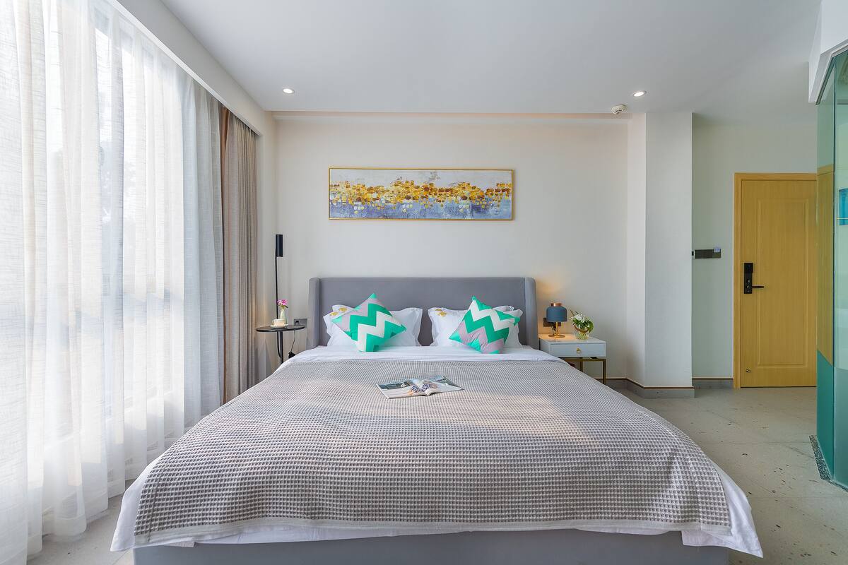 Una cama bien hecha con una colcha a cuadros, dos almohadas con diseños en zigzag y un cuadro sobre la cama.