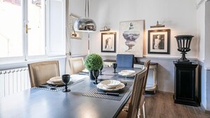 Una sala da pranzo con un tavolo lungo, sedie, una pianta in vaso e quadri appesi al muro.