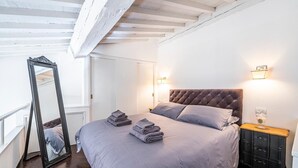 Una camera da letto con una testiera trapuntata, un grande specchio e un comodino con una lampada.