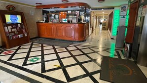 Un hall d’entrée comprenant un comptoir d’enregistrement, un bureau d’accueil et un panneau indicateur menant au bar et à la cafétéria.