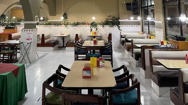 Un restaurant avec des banquettes et des tables, un sol carrelé et un présentoir à menus.