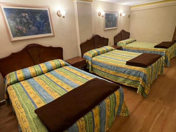 A hotel room with three beds, each with a striped bedspread and a brown pillow. There are wall-mounted light fixtures and a painting above the beds. - HOTEL MARIA CRISTINA (San Luis Potosí)