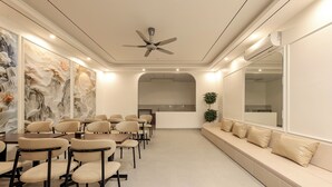 Une salle de conférence moderne, dotée d’un ventilateur de plafond, d’une longue table entourée de chaises, d’un canapé avec des coussins et d’un grand miroir mural.