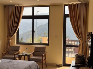 A hotel room with a bed, two armchairs, a small table with a teapot and glasses, and a large window with curtains. - Merit Sapa Hotel (Sa Pa)