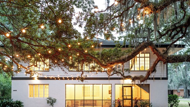 Un edificio blanco con ventanas amplias y un árbol en la parte delantera.