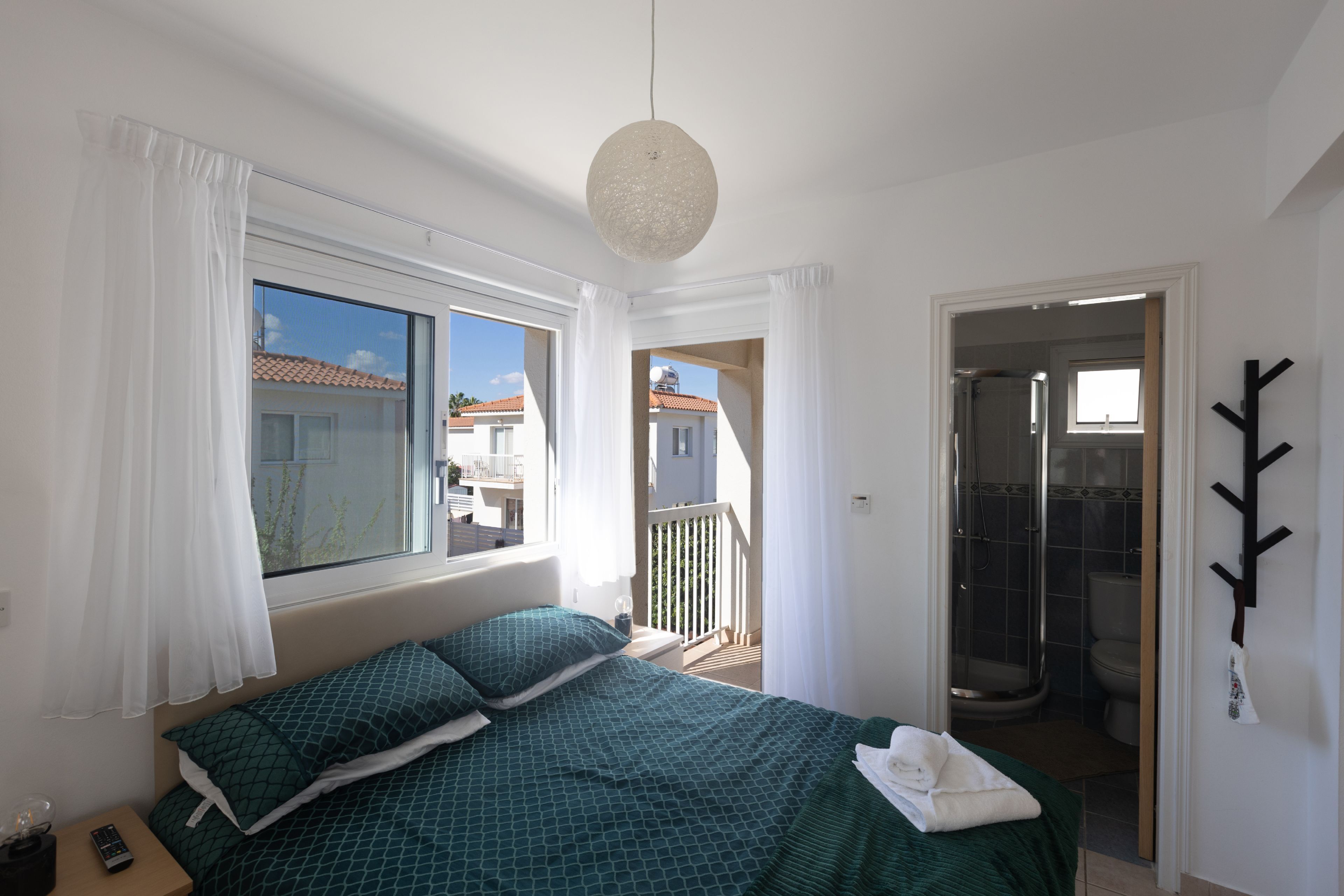 A bedroom with a bed, curtains, a hanging light fixture, and a view of the outside.
