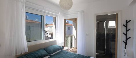 A bedroom with a bed, curtains, a hanging light fixture, and a view of the outside.