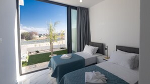 A hotel room with two beds, a large window with a view of a garden and buildings, and a modern design.