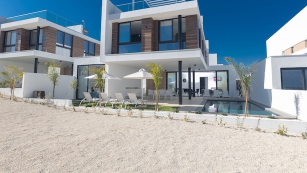 A modern multi-story building with a pool, outdoor seating, and a clear sky.