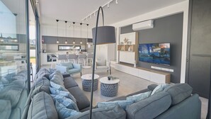 Una sala de estar moderna con un sofá grande, una zona de comedor y una cocina al fondo.