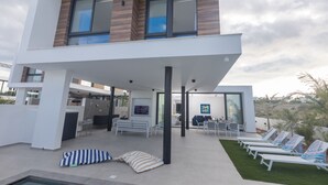 Una casa moderna de dos pisos con un área exterior techada, piscina y sillas de descanso.