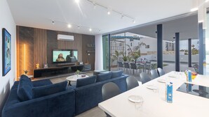 Una sala de estar moderna con un televisor grande, un sofá azul y un comedor con una mesa dispuesta para dos.
