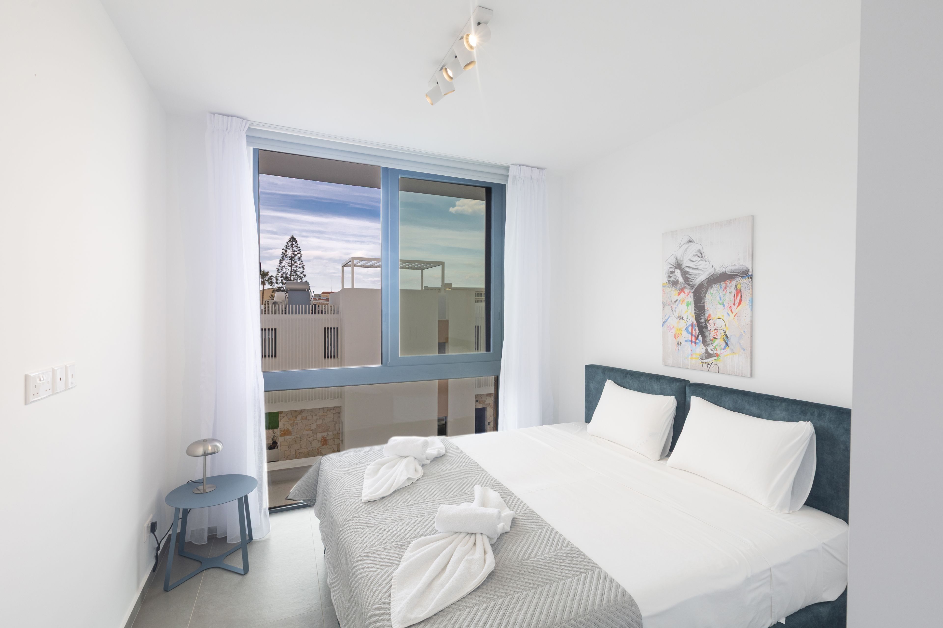 Una camera d'albergo moderna con un letto grande, un tavolino, una finestra con tende e un quadro appeso al muro.