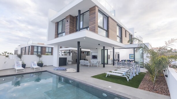 Una casa moderna de dos pisos con piscina, mobiliario exterior y un jardín bien cuidado.