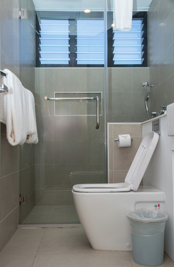 A modern bathroom with a glass-enclosed shower, a white toilet, a towel rack, and a trash bin.