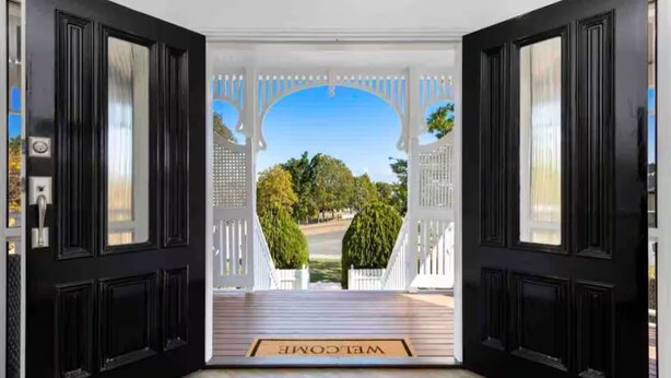 A black door with a white porch leading to a view of a street and trees.
