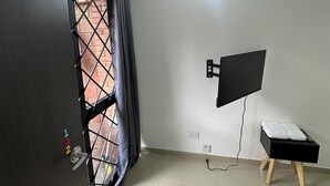 A room with a door, a TV mounted on the wall, a small wooden stool, and a power outlet. - BAMUKA HOSTEL (Bogotá)