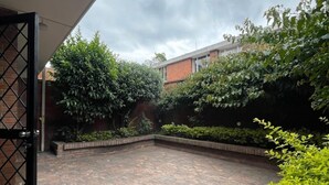 A courtyard with a tiled floor, surrounded by greenery and a brick wall. - BAMUKA HOSTEL (Bogotá)