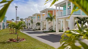 A row of modern, two-story beachfront hotels with balconies, a paved walkway, and palm trees. - New Waterfront❗️Pool, Epic Views/Corner Lot❤️Beaches near~BBQ Grill~Washer/Dryer (Jensen Beach)