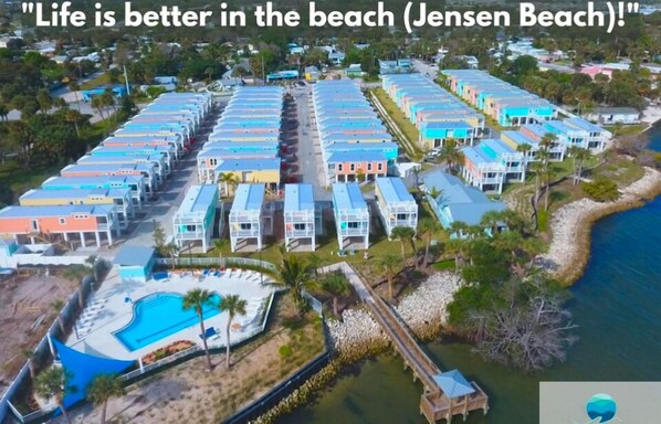 Ett flygbildsbild av ett semesterområde med färgglada byggnader, en swimmingpool och en strand.