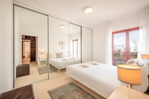 Ein modernes Hotelzimmer mit einem großen Bett, einer Sitzecke mit einem Sessel, einem Schreibtisch und einem großen Fenster mit Blick auf die Stadt.