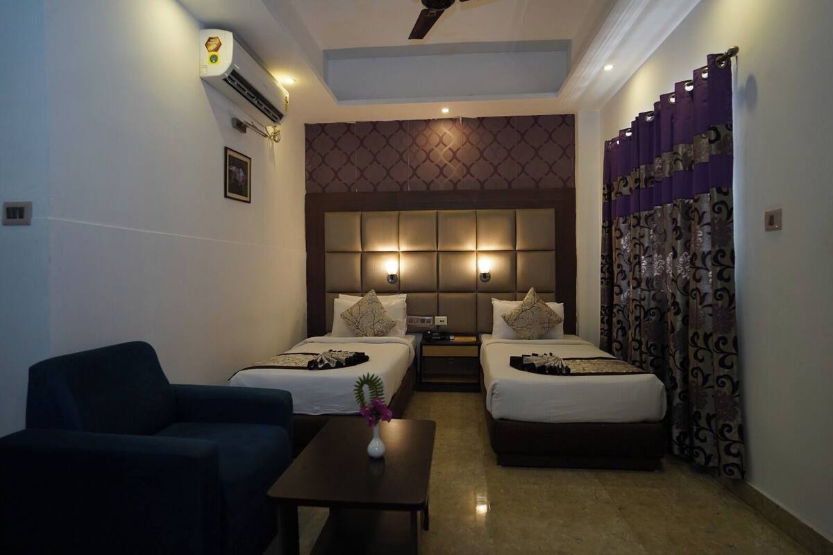 A hotel room with two beds, a sofa, a small table, and a ceiling fan.