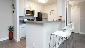 A modern kitchen with white cabinets, stainless steel appliances, and a central island with bar stools. - Charming 2-bedroom Apt with Rooftop Pool & Hollywood Sign View (Los Angeles)