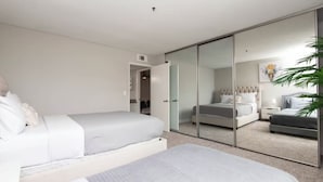 A modern bedroom with a large bed, a smaller bed, a wardrobe with a mirror, and a plant. - Charming 2-bedroom Apt with Rooftop Pool & Hollywood Sign View (Los Angeles)