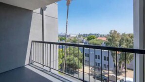 A balcony with a metal railing, a clear view of the surrounding buildings, and a tall palm tree. - Charming 2-bedroom Apt with Rooftop Pool & Hollywood Sign View (Los Angeles)