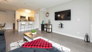 A modern living room with a sofa, a coffee table, and a TV mounted on the wall. - Charming 2-bedroom Apt with Rooftop Pool & Hollywood Sign View (Los Angeles)